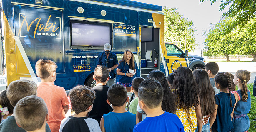 Professor Michele Nishiguchi talks to a group of Plainsburg Elementary School students at a science outreach event.